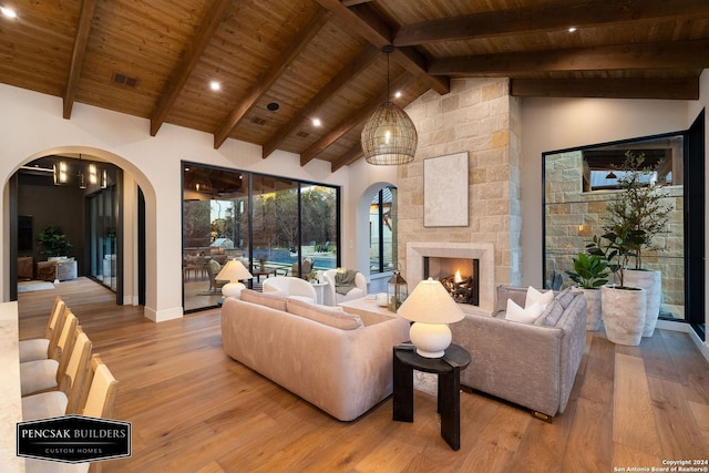 living room with beamed ceiling, light hardwood / wood-style floors, a stone fireplace, and wood ceiling