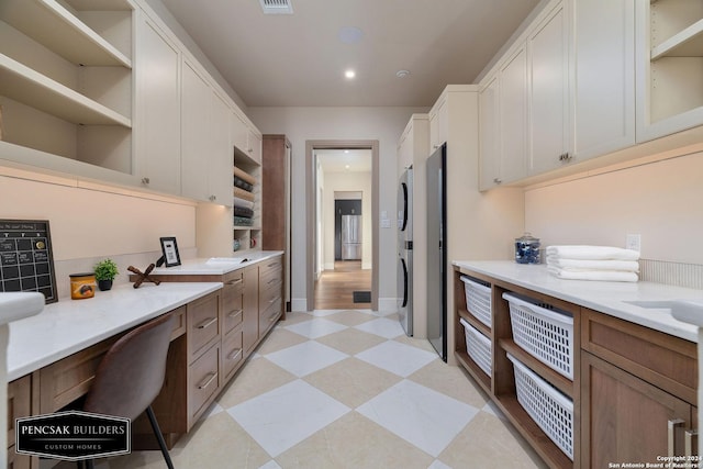 kitchen with white cabinets, built in desk, and stacked washer and clothes dryer