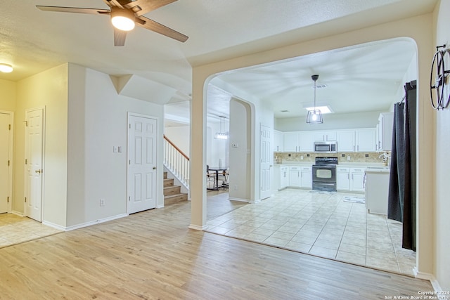 kitchen featuring decorative backsplash, black stove, pendant lighting, white cabinets, and light hardwood / wood-style floors