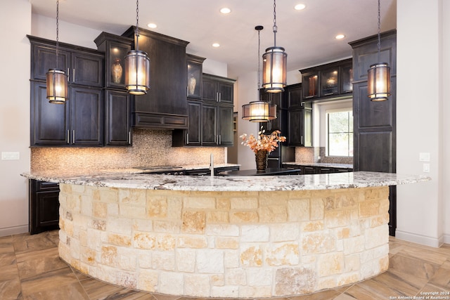 kitchen with decorative backsplash, decorative light fixtures, light stone counters, and a large island