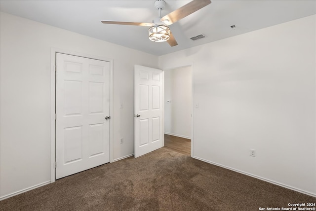 unfurnished bedroom with ceiling fan, a closet, and dark colored carpet