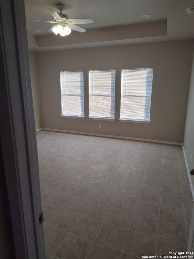 tiled spare room featuring a raised ceiling and ceiling fan