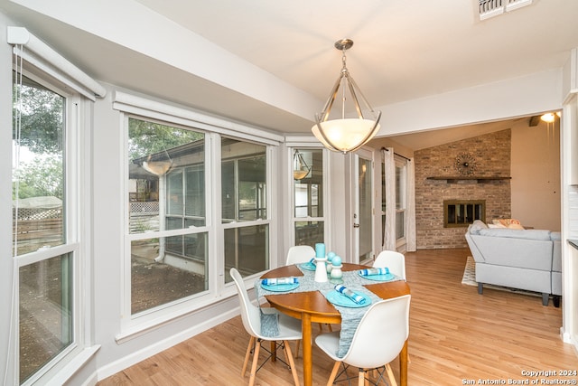 dining space with hardwood / wood-style flooring, vaulted ceiling, and a brick fireplace