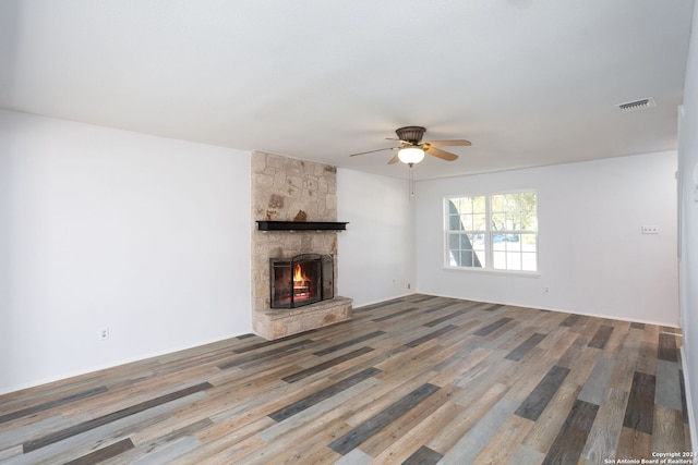 unfurnished living room with hardwood / wood-style floors, a stone fireplace, and ceiling fan