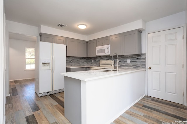 kitchen with kitchen peninsula, white appliances, light hardwood / wood-style floors, and sink