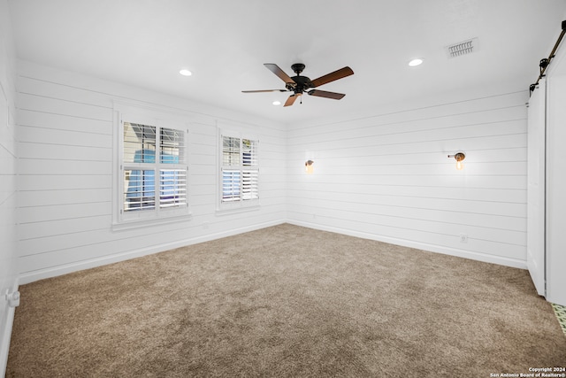 carpeted spare room featuring a barn door, ceiling fan, and wooden walls