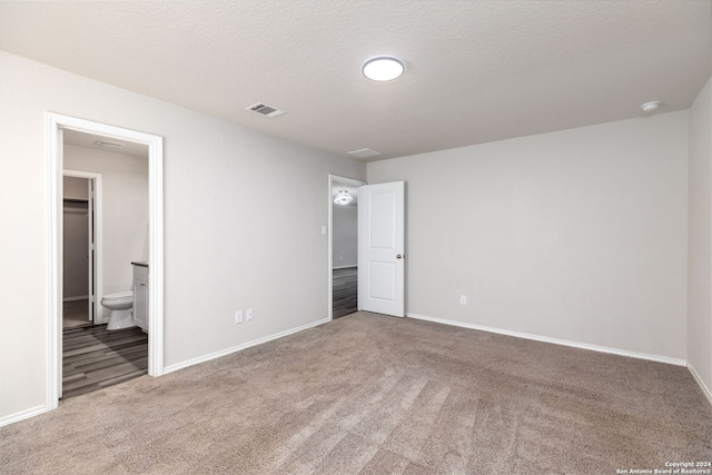 unfurnished bedroom with carpet flooring, connected bathroom, and a textured ceiling