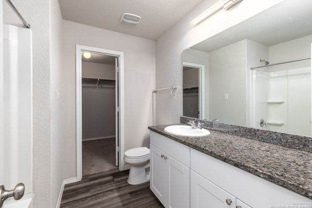 bathroom featuring vanity, hardwood / wood-style flooring, toilet, walk in shower, and a textured ceiling