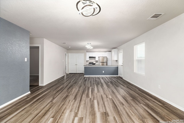 unfurnished living room with a chandelier, dark wood-type flooring, and a textured ceiling