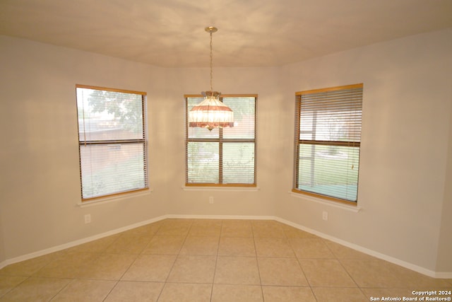 tiled spare room with an inviting chandelier