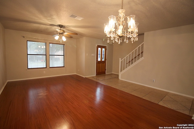 unfurnished living room featuring ceiling fan with notable chandelier, wood-type flooring, a textured ceiling, and plenty of natural light