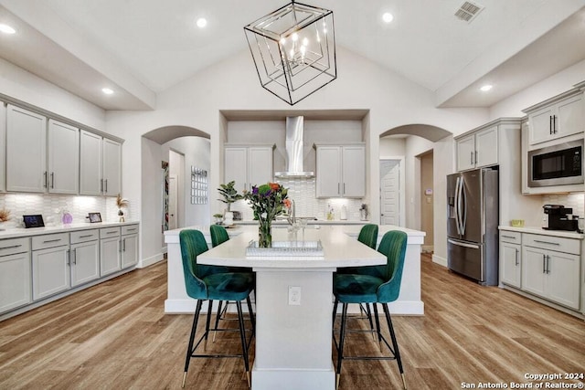 kitchen with decorative backsplash, lofted ceiling, wall chimney range hood, and appliances with stainless steel finishes