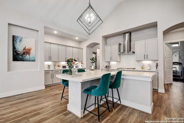 kitchen featuring hanging light fixtures, a breakfast bar, a kitchen island with sink, and wall chimney range hood