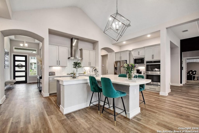 kitchen with a kitchen breakfast bar, a kitchen island with sink, wall chimney exhaust hood, and appliances with stainless steel finishes