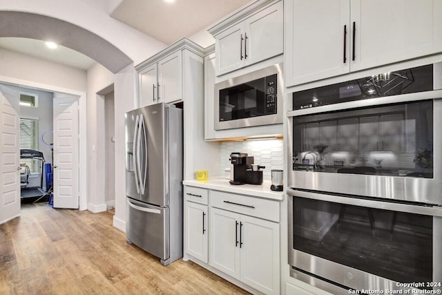 kitchen with white cabinets, decorative backsplash, stainless steel appliances, and light hardwood / wood-style flooring