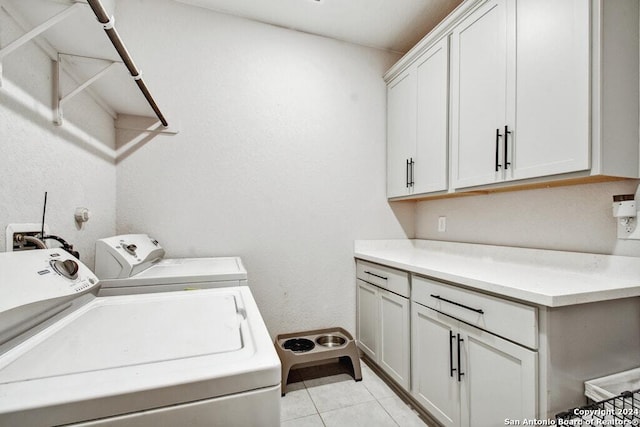 clothes washing area with cabinets, light tile patterned floors, and washing machine and clothes dryer