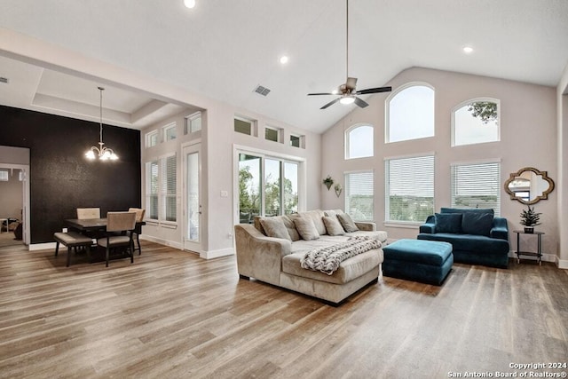 living room with ceiling fan with notable chandelier, light hardwood / wood-style floors, and high vaulted ceiling