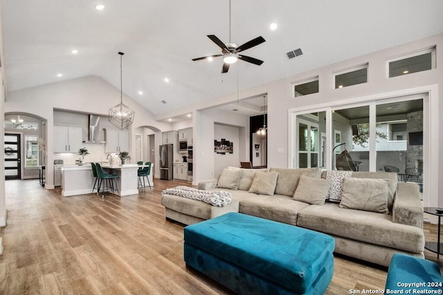 living room featuring high vaulted ceiling, ceiling fan with notable chandelier, and light wood-type flooring