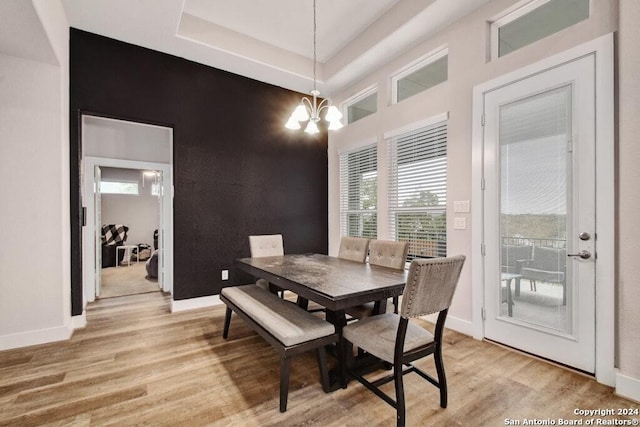 dining space with a chandelier, light wood-type flooring, and a raised ceiling