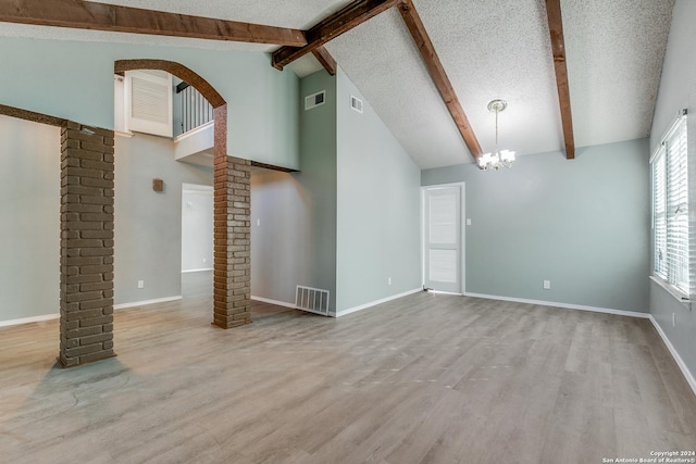 unfurnished living room with ornate columns, a textured ceiling, a notable chandelier, beamed ceiling, and light hardwood / wood-style floors