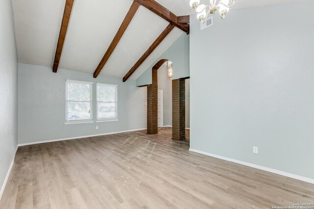 unfurnished living room featuring decorative columns, an inviting chandelier, lofted ceiling with beams, and light wood-type flooring