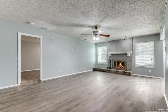 unfurnished living room with hardwood / wood-style floors, a textured ceiling, and a brick fireplace