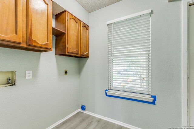 clothes washing area with cabinets, electric dryer hookup, hookup for a washing machine, a textured ceiling, and light wood-type flooring