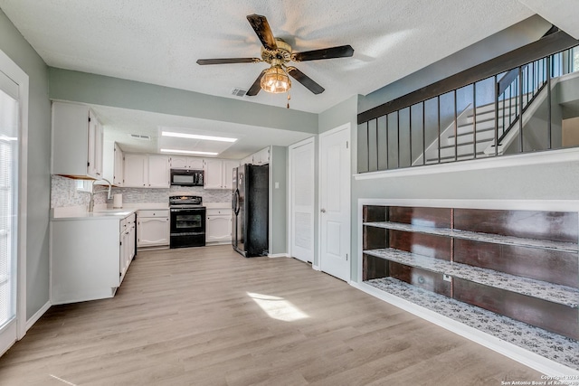 kitchen featuring light wood-type flooring, tasteful backsplash, sink, black appliances, and white cabinetry