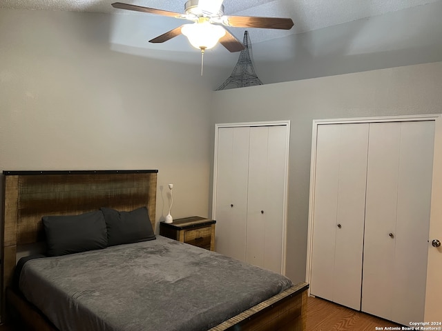 bedroom with lofted ceiling, ceiling fan, a textured ceiling, light hardwood / wood-style floors, and multiple closets