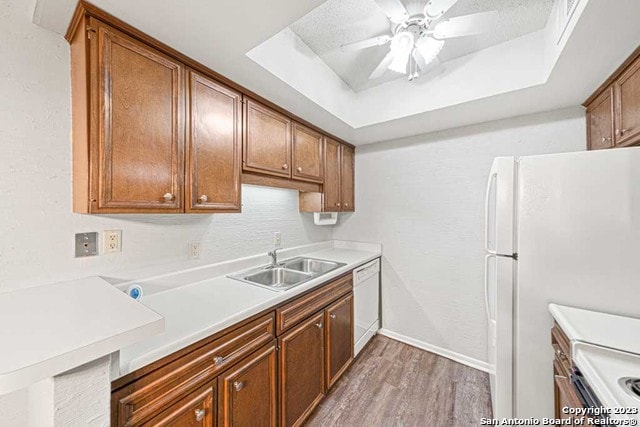 kitchen with white appliances, sink, ceiling fan, a tray ceiling, and wood-type flooring