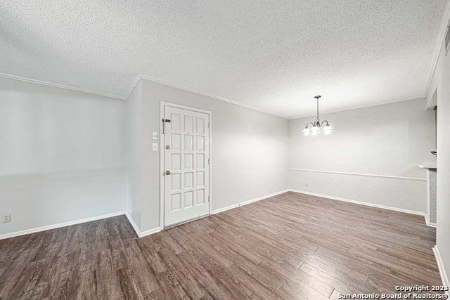 spare room featuring dark hardwood / wood-style floors, crown molding, a textured ceiling, and an inviting chandelier