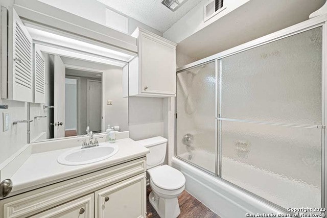 full bathroom featuring vanity, a textured ceiling, wood-type flooring, enclosed tub / shower combo, and toilet