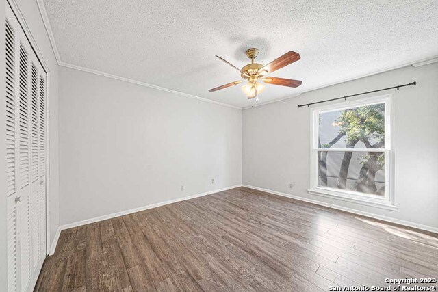 unfurnished bedroom featuring ornamental molding, a textured ceiling, ceiling fan, dark hardwood / wood-style floors, and a closet