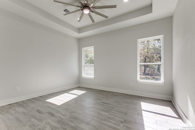 spare room featuring a raised ceiling, ceiling fan, plenty of natural light, and light hardwood / wood-style floors