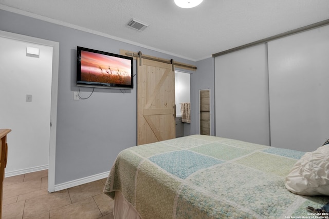 bedroom with a textured ceiling, crown molding, a barn door, tile patterned flooring, and a closet