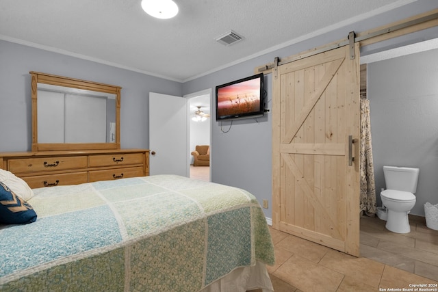 bedroom with ensuite bath, a textured ceiling, crown molding, light tile patterned floors, and a barn door