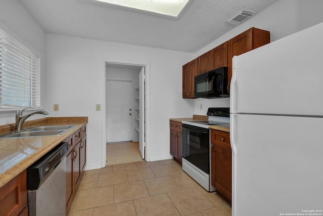 kitchen with light tile patterned flooring, a textured ceiling, white appliances, and sink