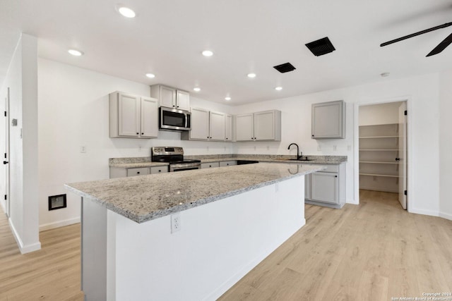 kitchen featuring gray cabinets, a kitchen island, stainless steel appliances, and light wood-type flooring