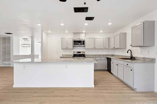 kitchen featuring sink, light stone countertops, light hardwood / wood-style floors, appliances with stainless steel finishes, and a kitchen island