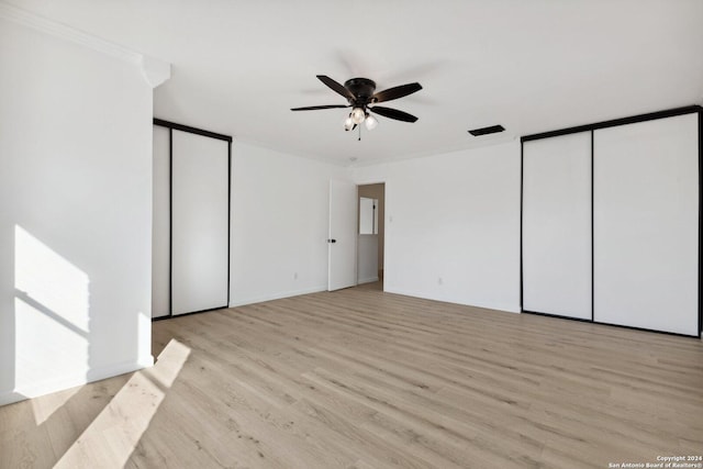 unfurnished bedroom featuring light hardwood / wood-style floors, crown molding, ceiling fan, and multiple closets