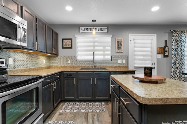 kitchen with sink, a center island, hanging light fixtures, appliances with stainless steel finishes, and light wood-type flooring