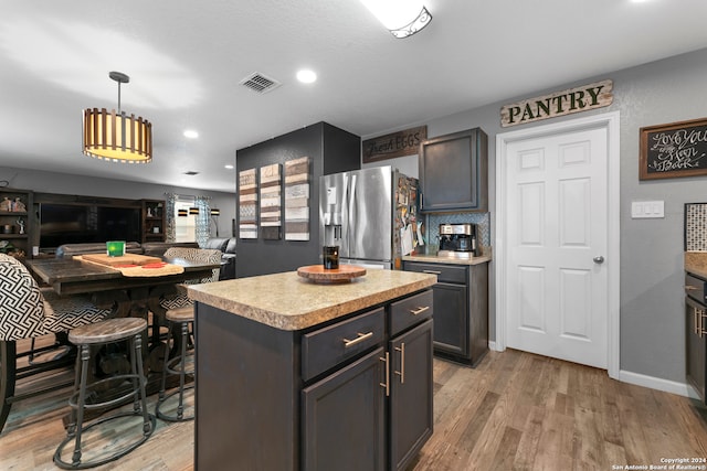 kitchen with dark brown cabinetry, a center island, hanging light fixtures, stainless steel fridge with ice dispenser, and light hardwood / wood-style floors