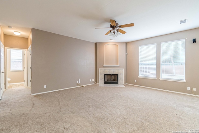 unfurnished living room featuring a tiled fireplace, ceiling fan, and light carpet