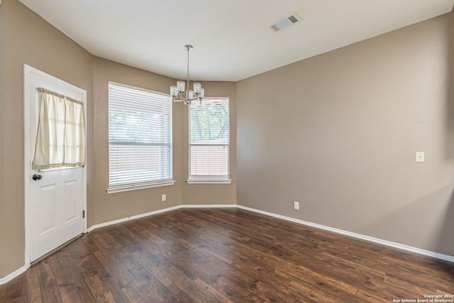 spare room with dark hardwood / wood-style floors and an inviting chandelier