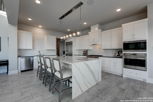 kitchen featuring white cabinets, hanging light fixtures, built in appliances, light stone counters, and a spacious island