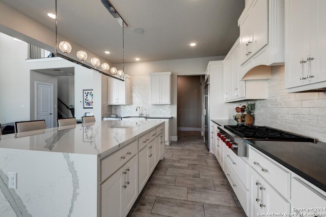 kitchen with pendant lighting, white cabinetry, a spacious island, dark stone counters, and stainless steel gas stovetop