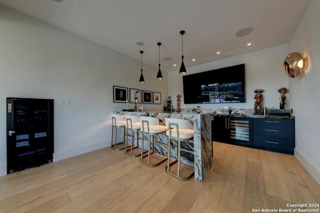 bar featuring wine cooler, decorative light fixtures, light stone countertops, and light hardwood / wood-style floors