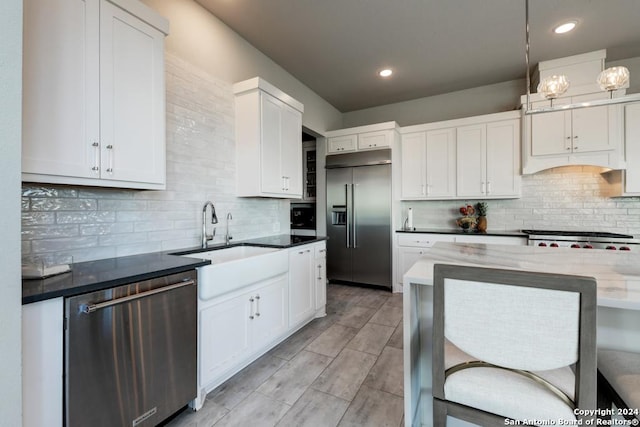 kitchen with sink, white cabinetry, dark stone countertops, appliances with stainless steel finishes, and pendant lighting