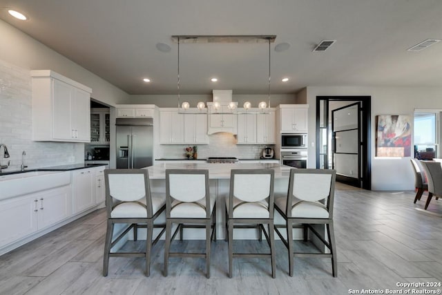 kitchen with decorative light fixtures, white cabinets, a kitchen breakfast bar, built in appliances, and a spacious island