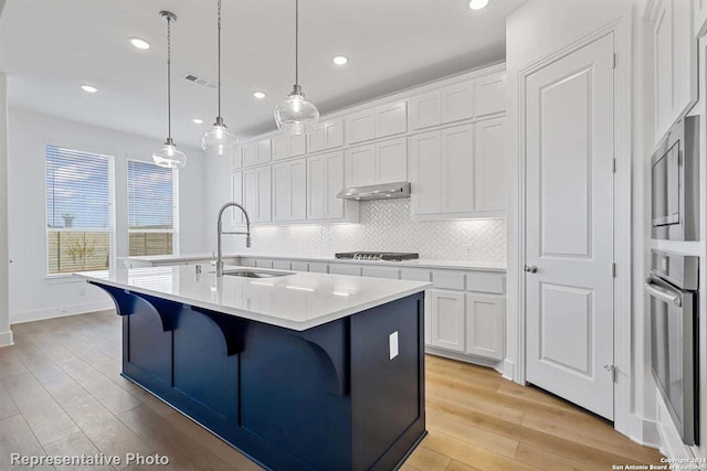 kitchen featuring appliances with stainless steel finishes, decorative light fixtures, white cabinetry, sink, and a center island with sink